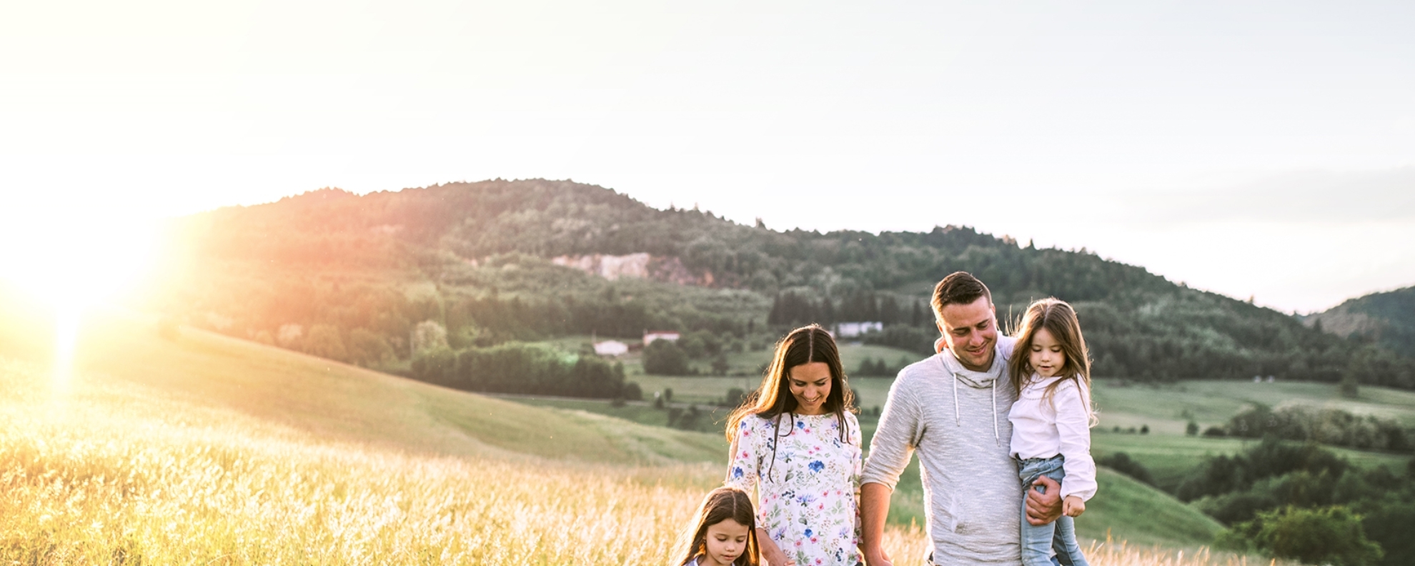 Portrait of a young father and mother with their daughters on a meadow on a sunny day.